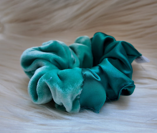 Two teal scrunchies on a textured beige surface