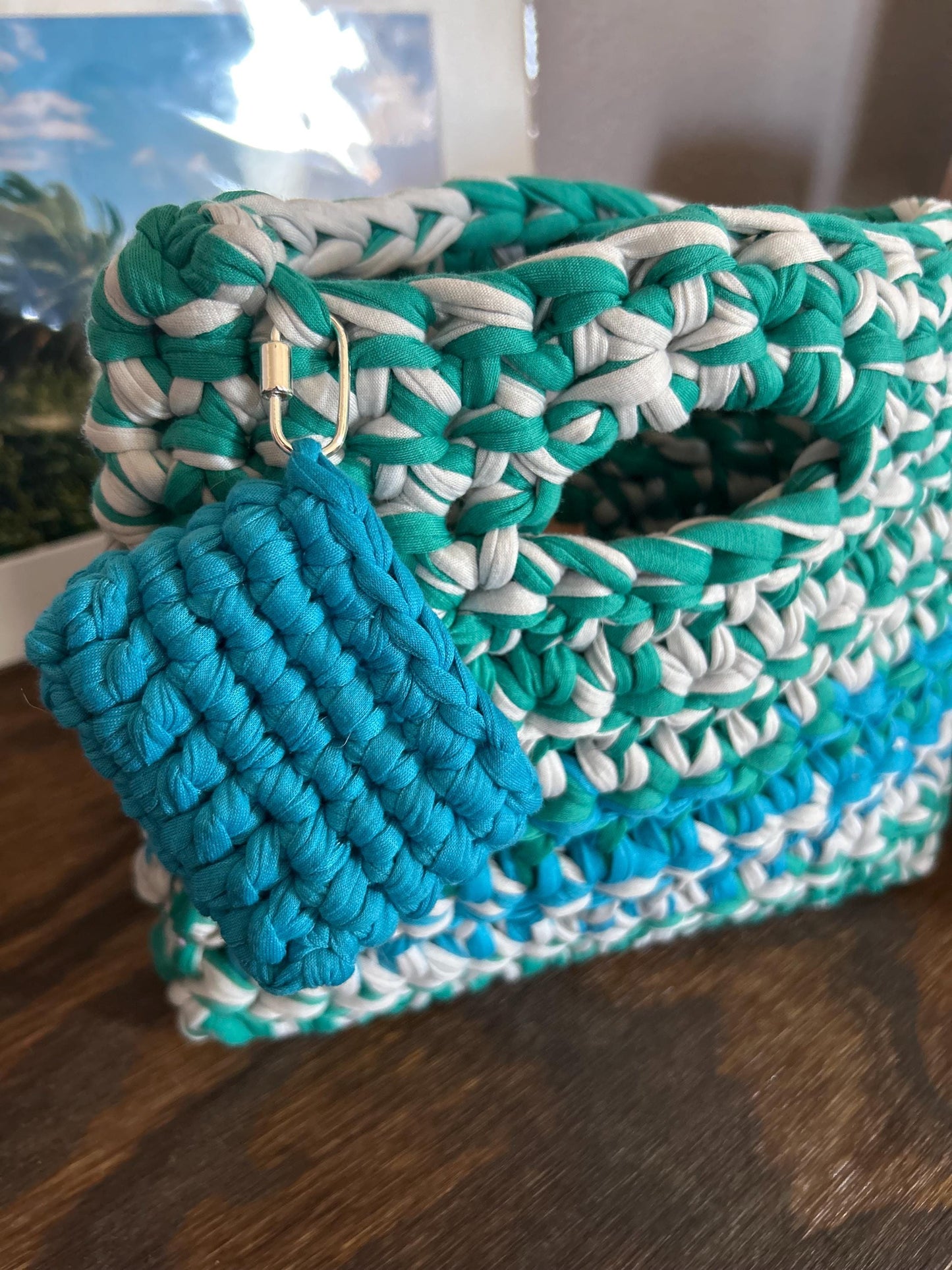 Teal and white crocheted clutch bag on a wooden surface