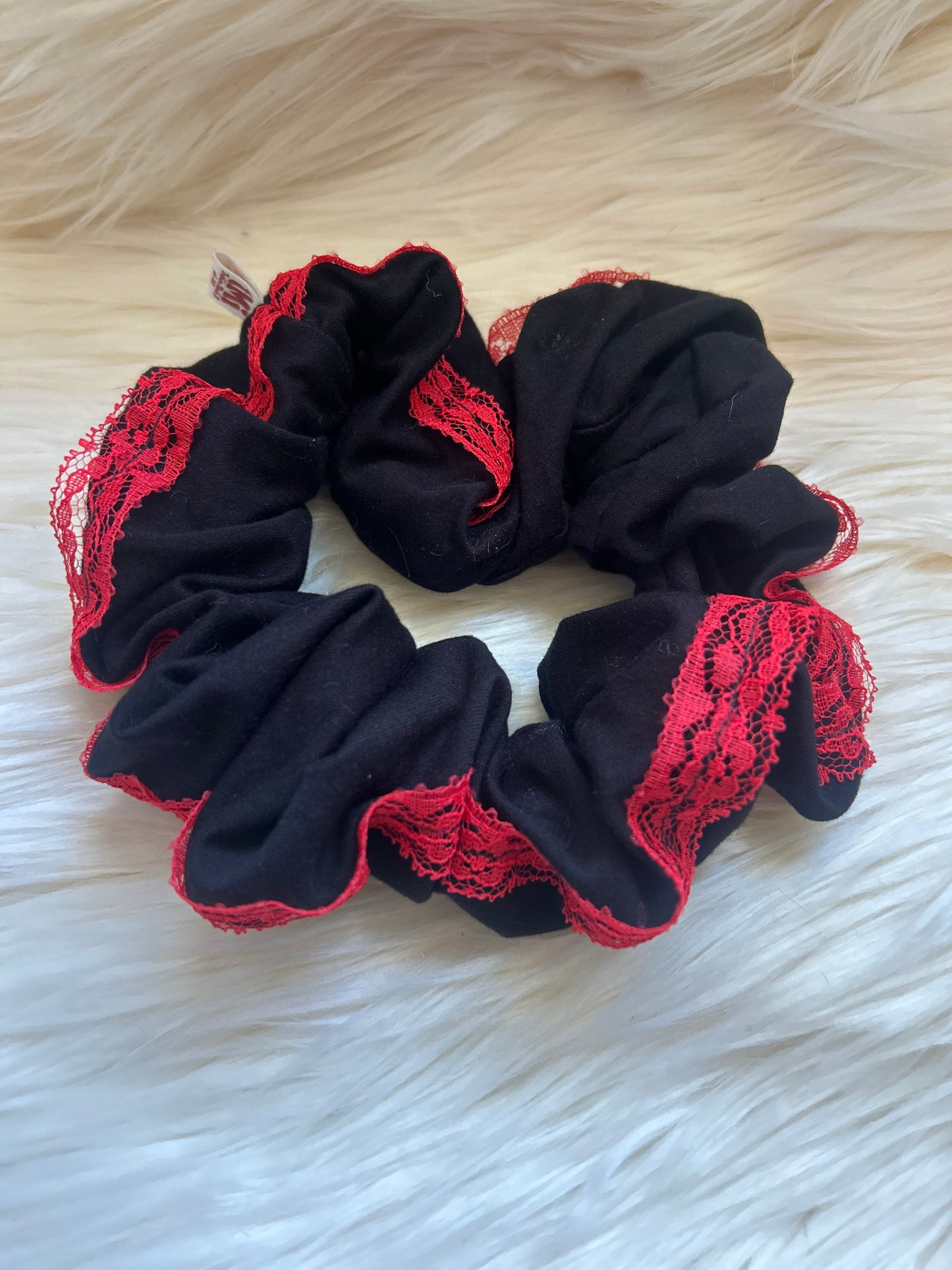 Black scrunchie with red lace details on a white fur background