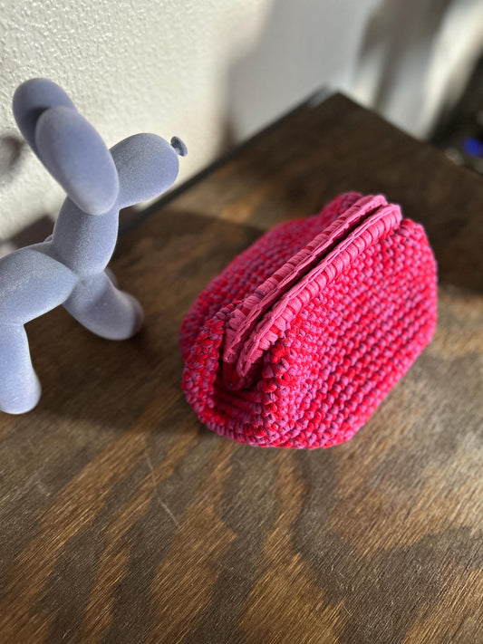 Pink crocheted pouch next to a blue balloon dog figure on a wooden surface.