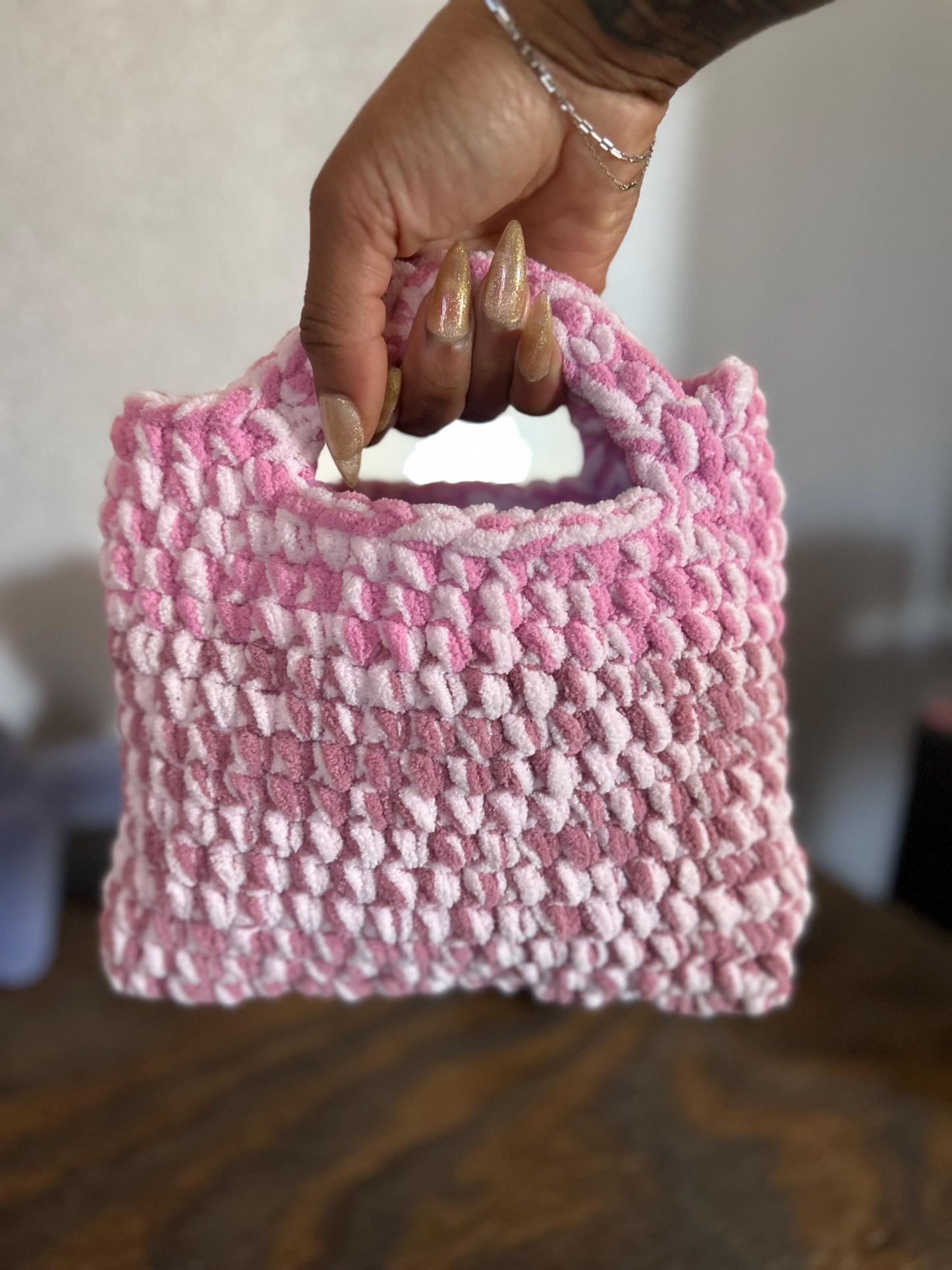 Hand holding a pink textured woven bag on a wooden surface with a blurred background
