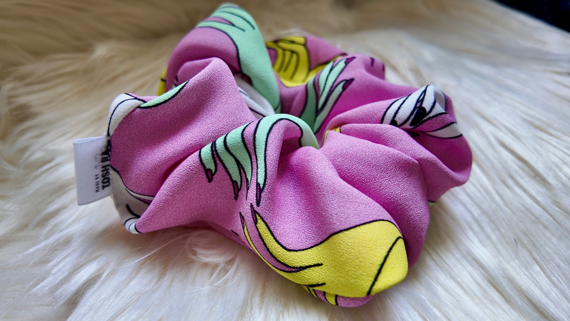 Pink scrunchie with colorful patterns on a white fluffy surface