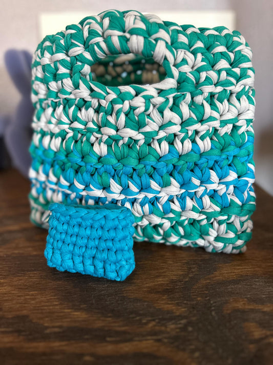 Crocheted shopper tote and square in teal, white, and blue on a wooden surface